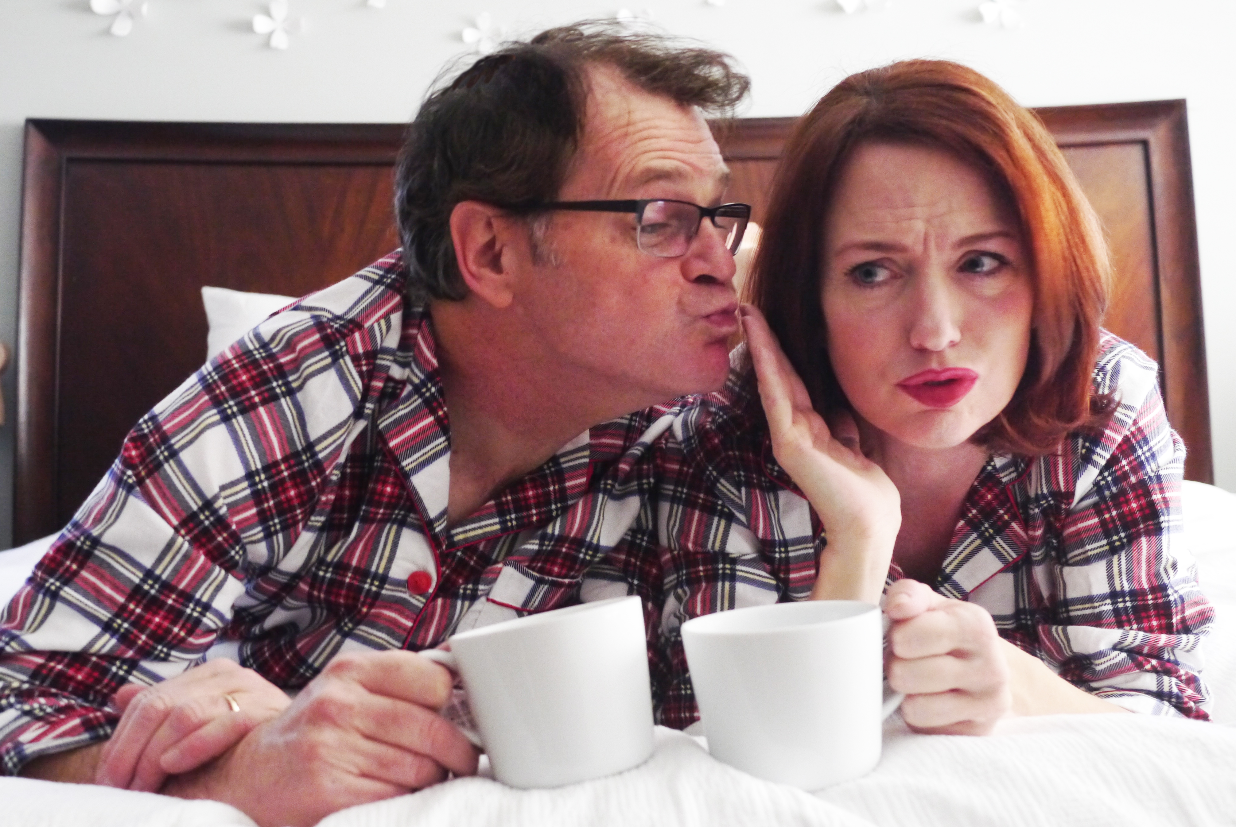 Two people laying on a bed with coffee mugs
