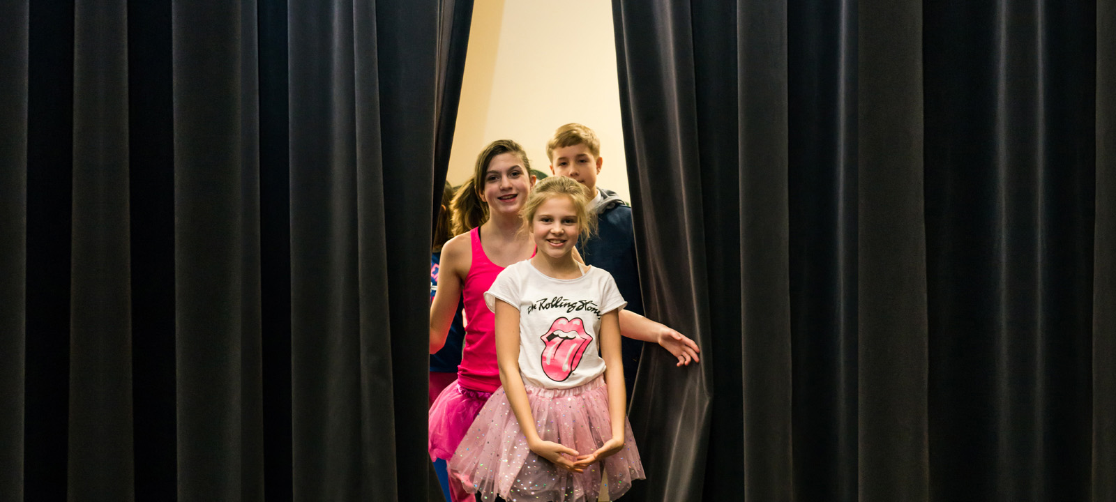 Girl standing at a theatre curtain on stage smiling